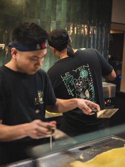Deux cuisiniers préparent des plats dans un restaurant asiatique Seiiki Le Yen avec une ambiance professionnelle en cuisine.