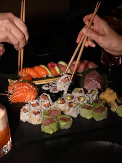 Plateau de sushi variés avec saumon, thon, rouleaux de riz et légumes, pris avec des baguettes dans un restaurant japonais.