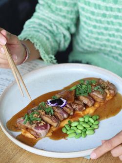 Plat asiatique avec tranches de viande nappées de sauce et accompagnées de fèves edamame sur une assiette blanche.