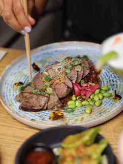 Bœuf tranché avec germes, oignons verts, edamames et légumes sur une assiette bleue à Seiiki Le Yen