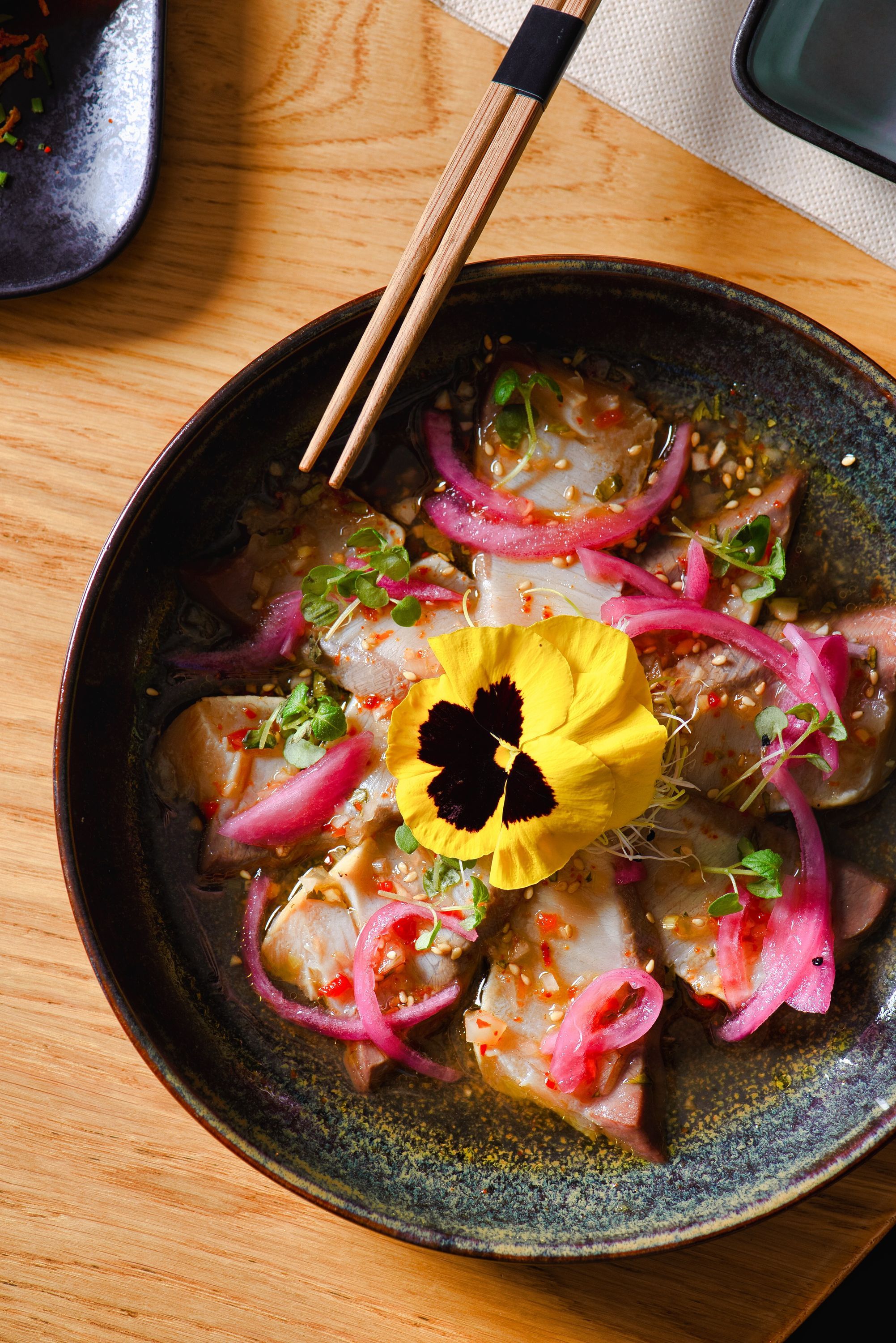 Plat artistique avec sashimi, garniture de fleurs comestibles, oignons rouges et graines de sésame.