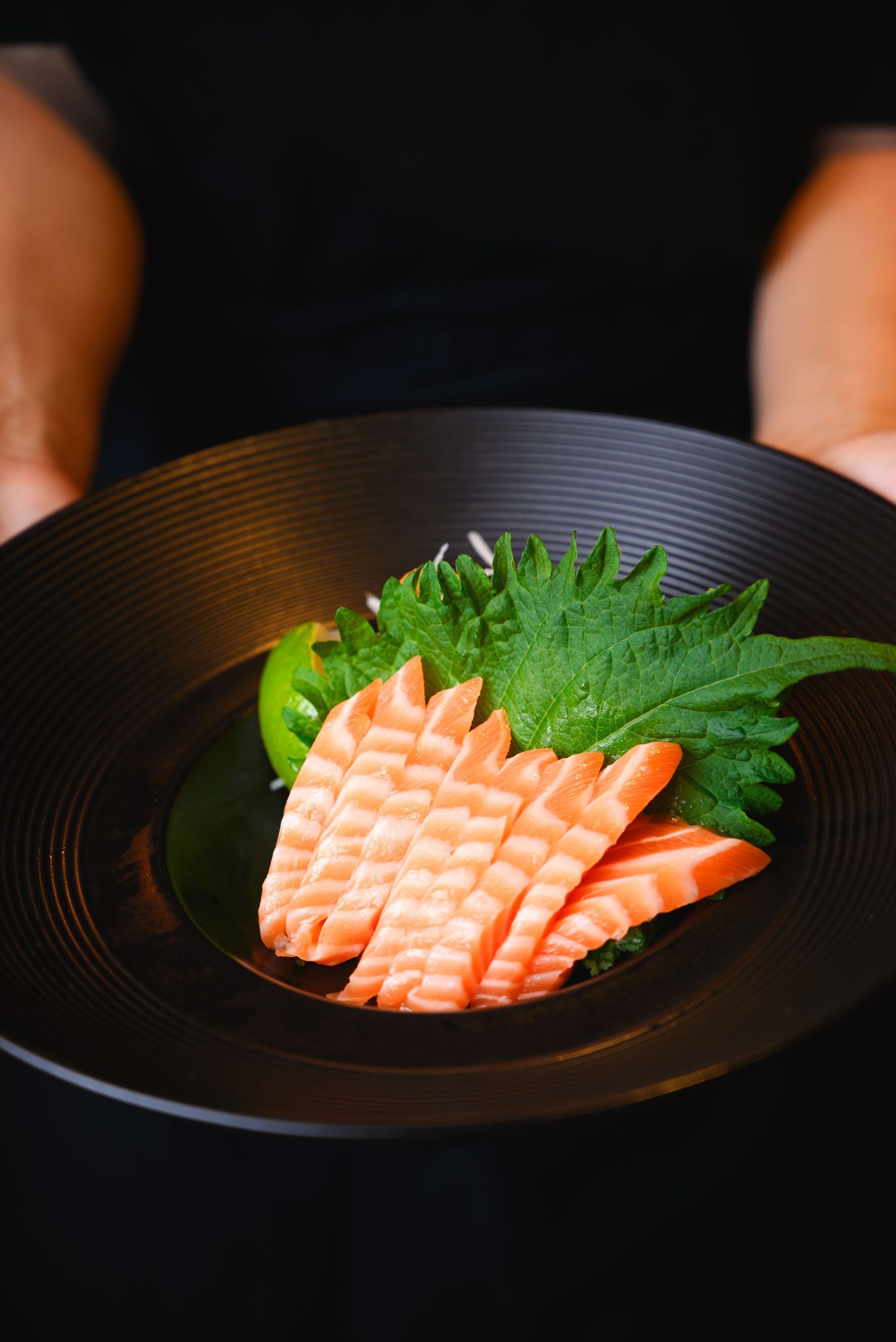 Découpage de saumon servi avec des garnitures sur une assiette noire.