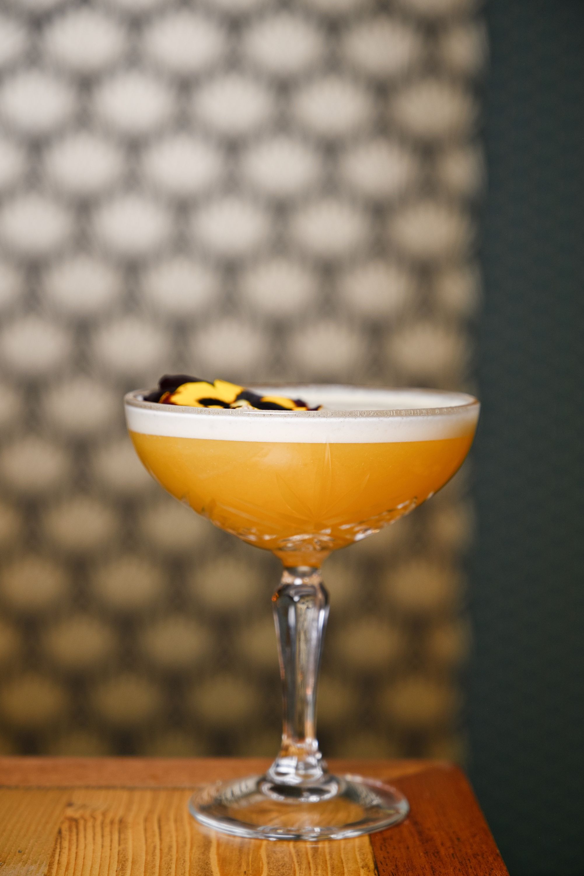 Un cocktail jaune servi dans un verre à champagne sur une table en bois.